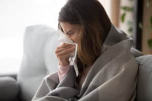 woman sitting with blanket freezing blowing running nose sneezing in tissue
