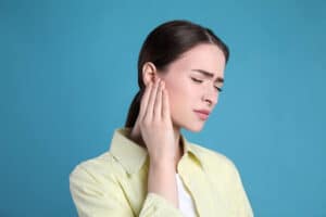 Young woman suffering from ear pain on light blue background Young woman suffering from ear pain on light blue background