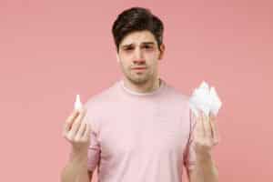 A man struggling with sinusitis holding tissues and eye drops